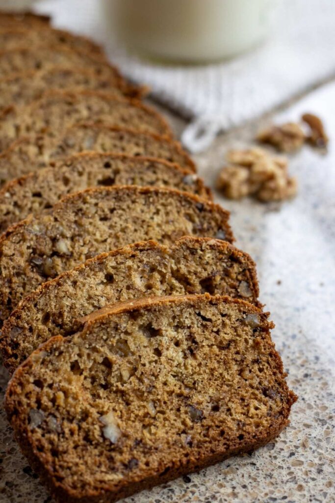 Slices of sourdough banana bread laid down on each other in a row with some walnuts in the background.