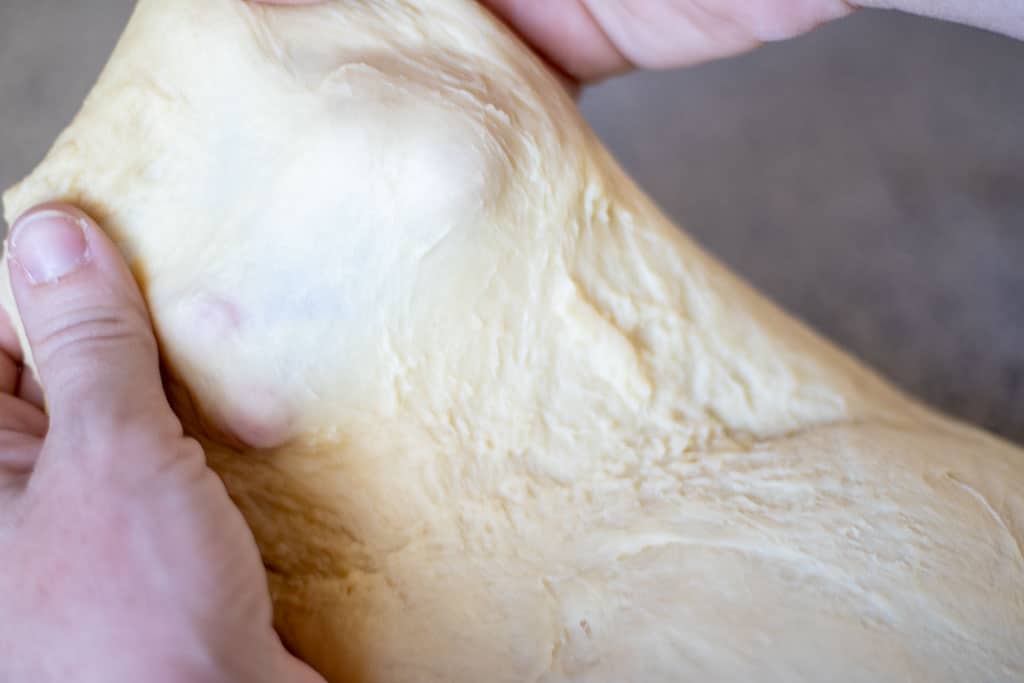 Hands stretching bread dough performing a window pane test.