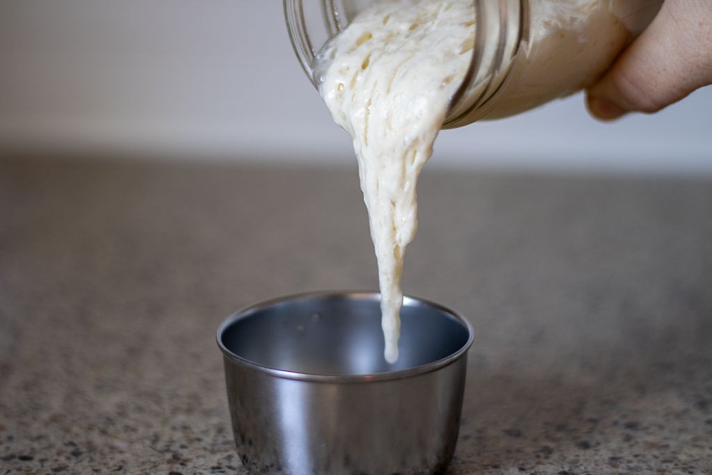 A woman pouring sourdough starter into a measuring cup.