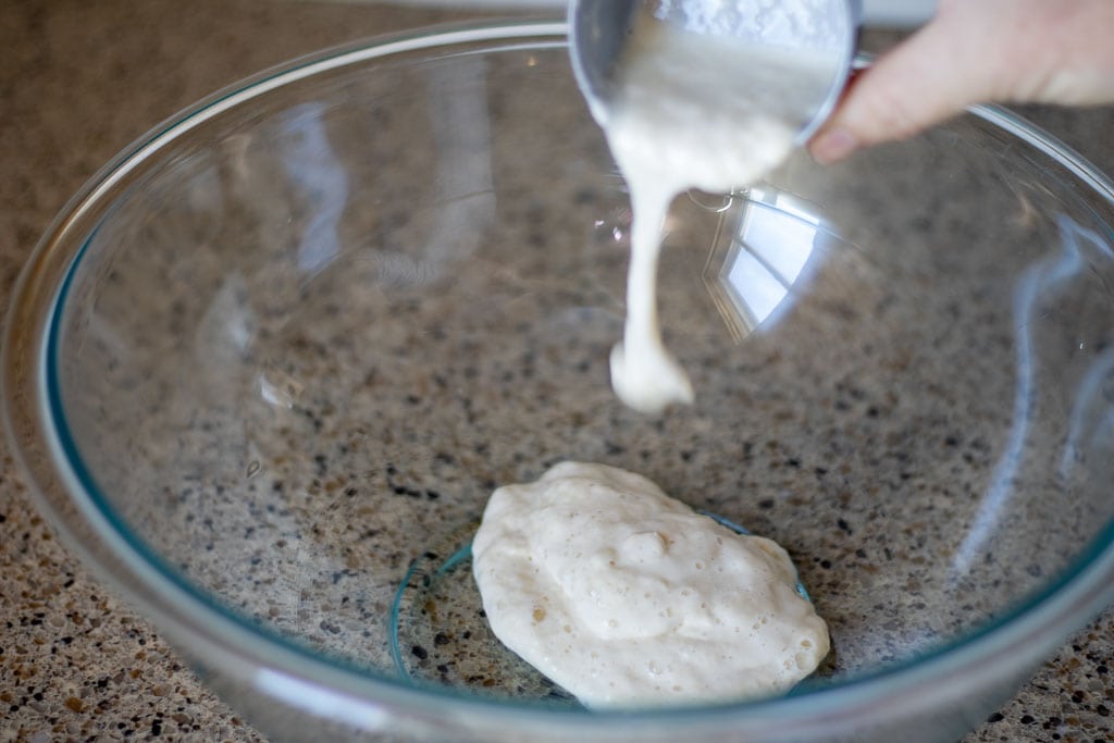 A woman pouring sourdough starter into a large glass bowl.