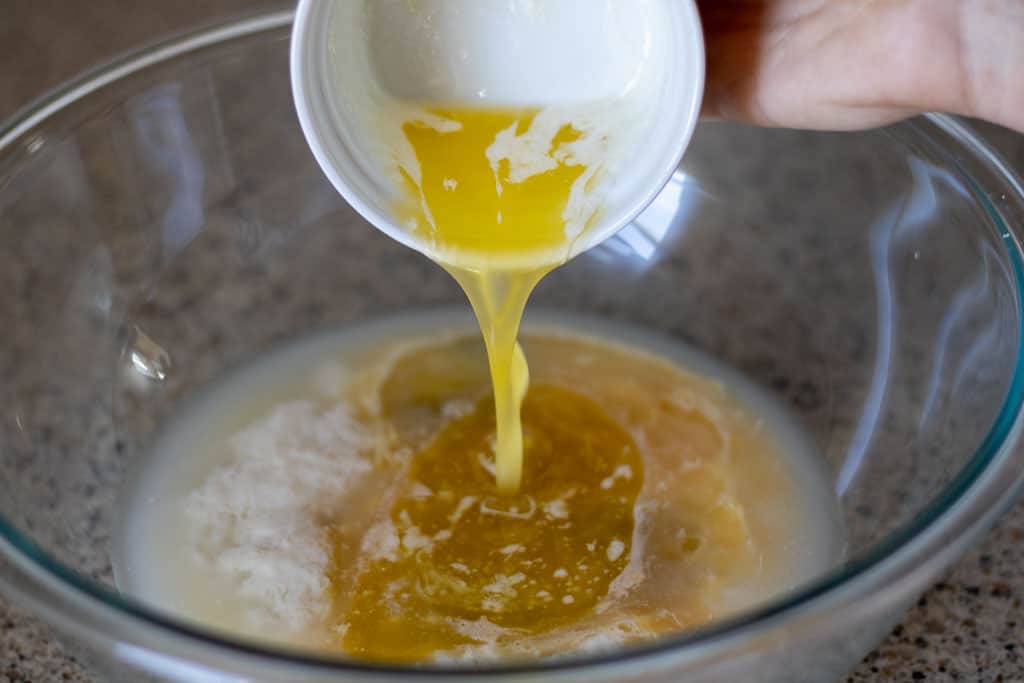 Pouring melted butter into a bowl of bread dough ingredients.