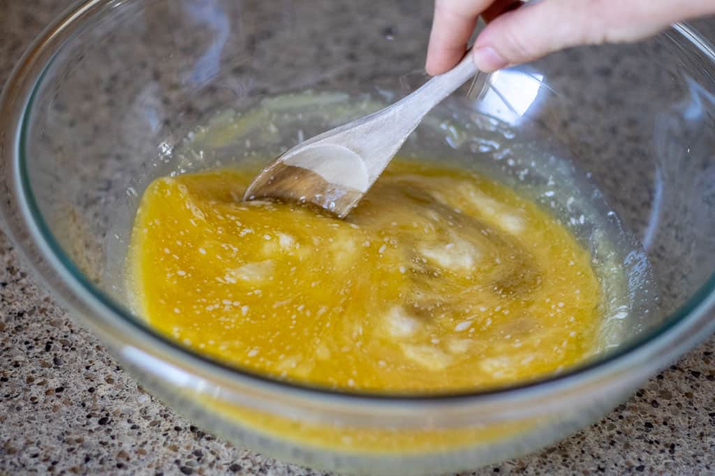 A hand mixing the wet bread dough ingredients with a wooden spoon.