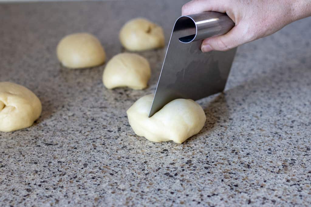 A hand cutting balls of bread dough into smaller portions.