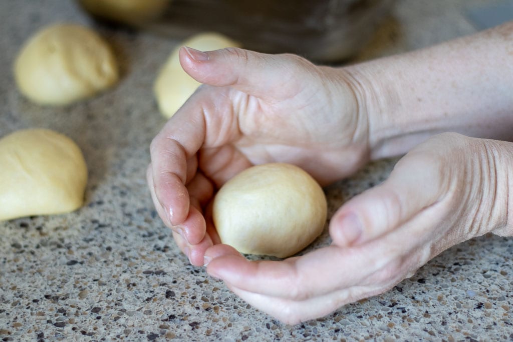 Hands shaping and rolling small balls of bread dough.