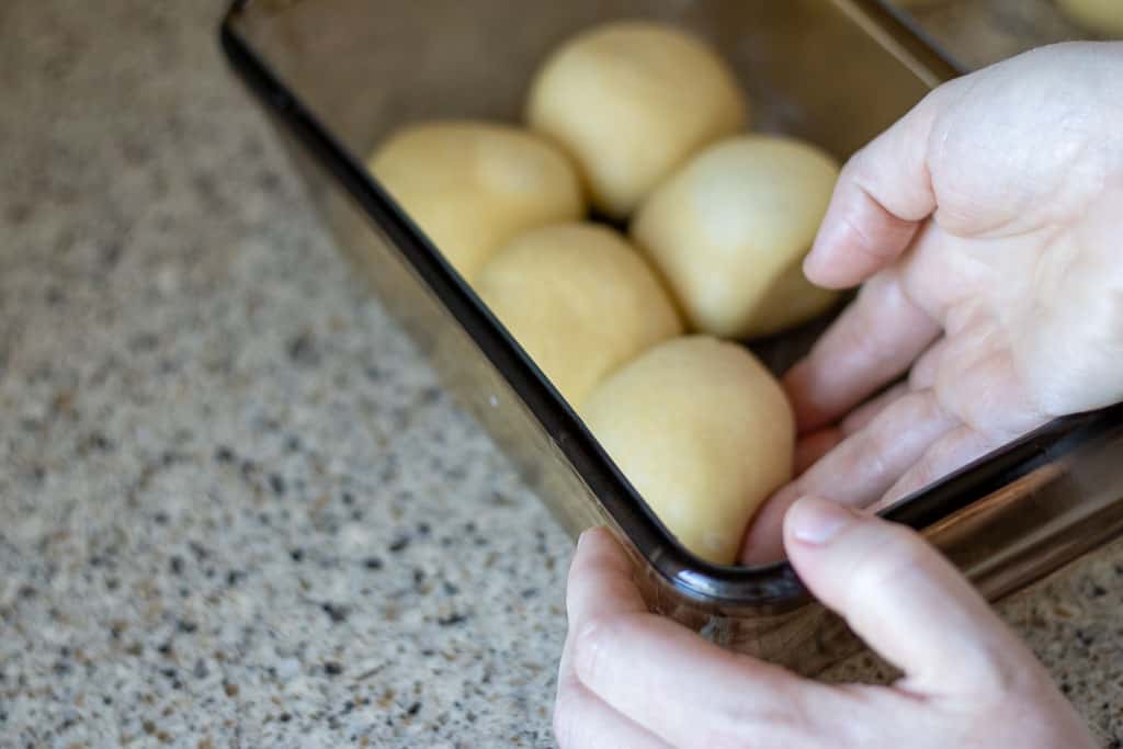 A hand placing small balls of challah dough into a greased loaf pan.