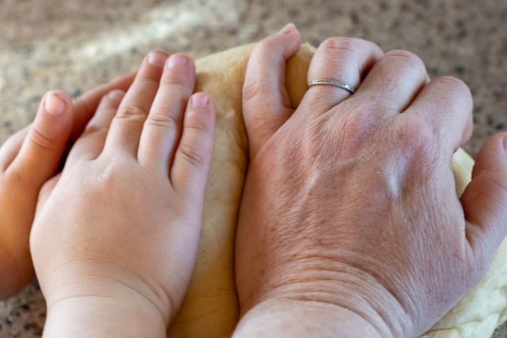 A mother and daughter kneading a dough ball by hand.