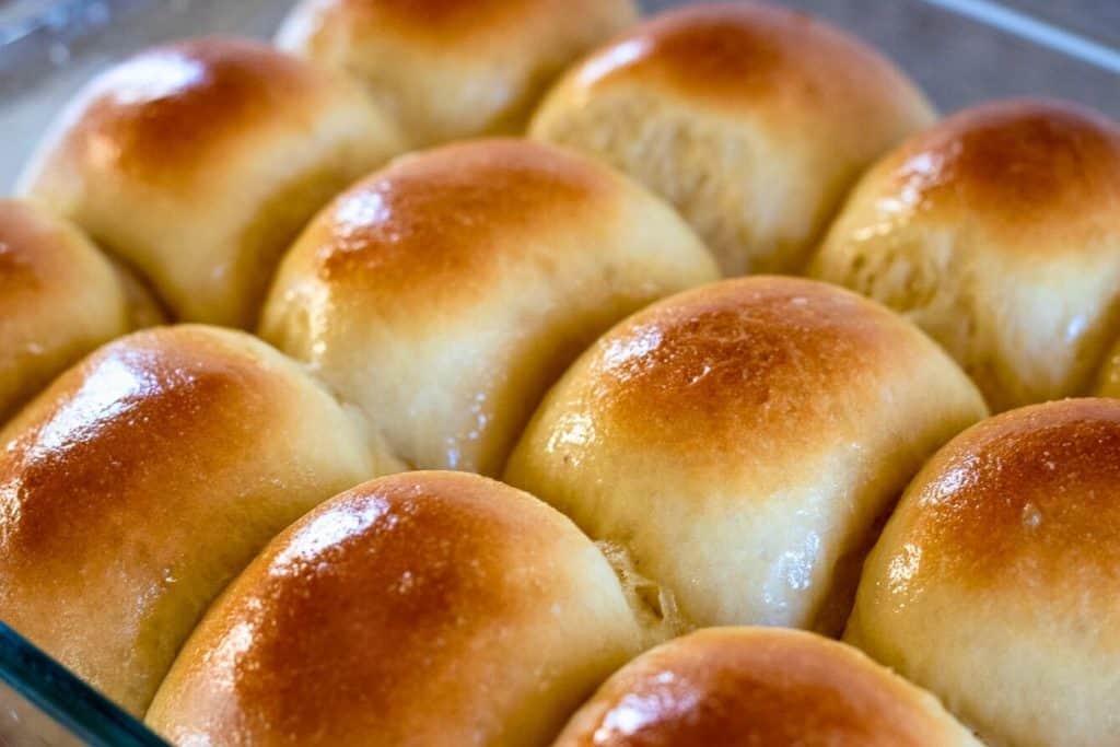 A baking pan full of freshly baked and buttered sourdough discard dinner rolls.