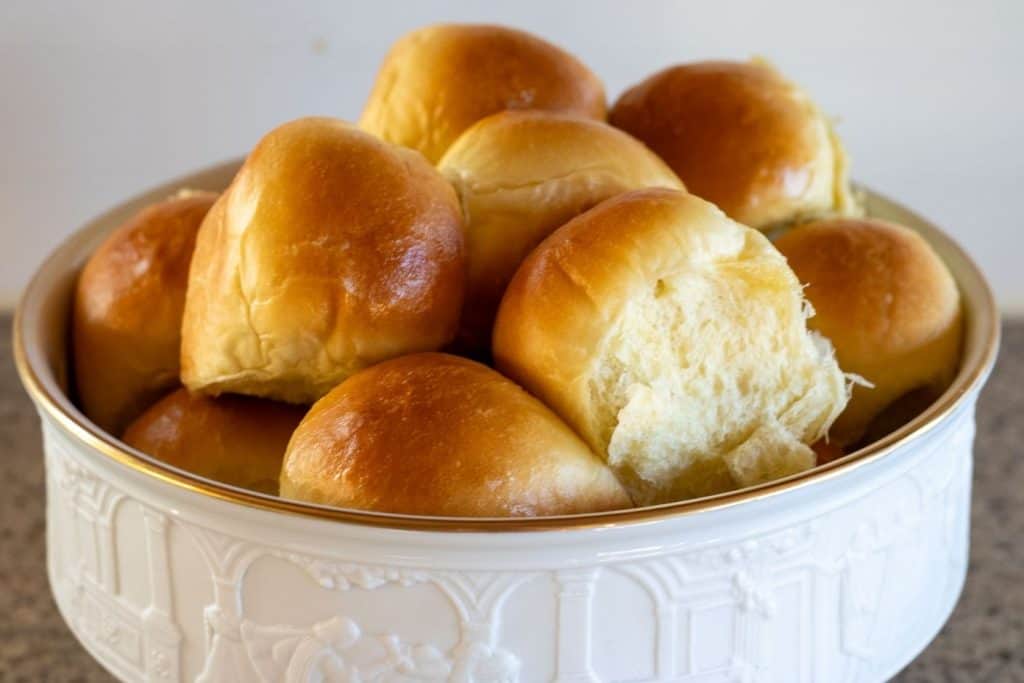 A bowl filled with buttered sourdough discard rolls.