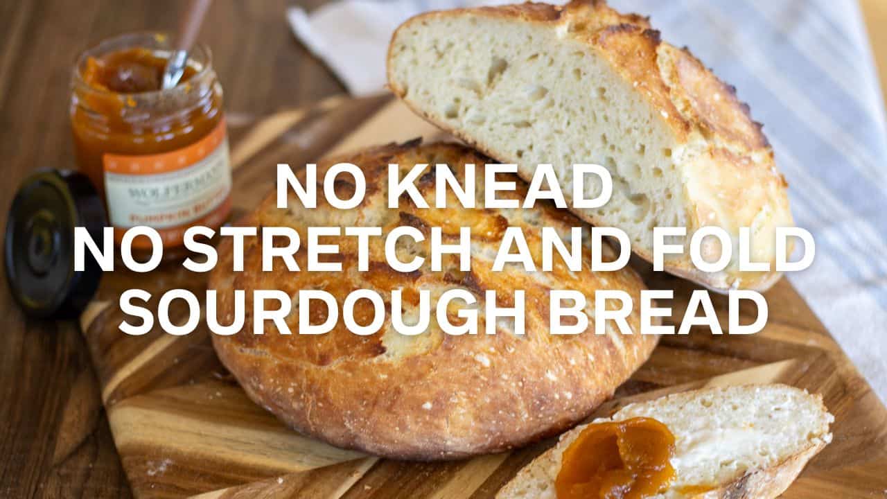A loaf of sourdough bread cut in half and set atop another loaf of bread on a cutting board with jam and butter.