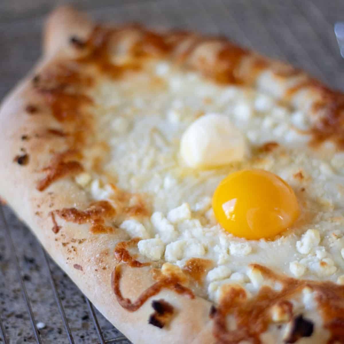 A baked Khachapuri bread boat on a wire rack.