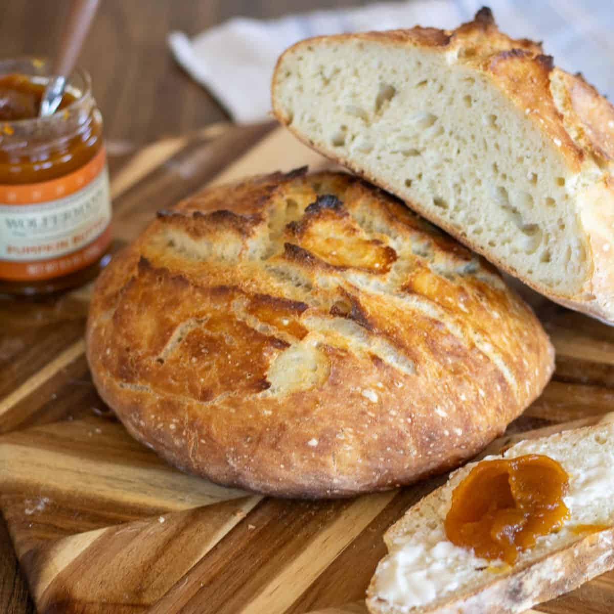A loaf of no knead no stretch and fold sourdough bread on a cutting board with jam and butter.