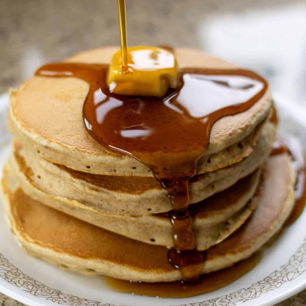 A stack of sourdough banana pancakes with maple syrup drizzled on top and a pat of butter.