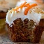 A sourdough carrot cake muffin with cream cheese frosting topped with shredded carrots for garnish and golden sprinkles.