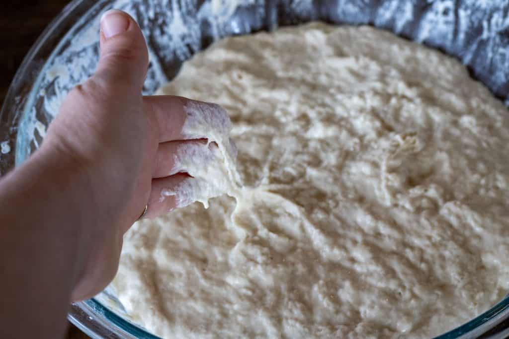 A hand with sticky dough stuck to her fingers showing the consistency of a wet sourdough dough.