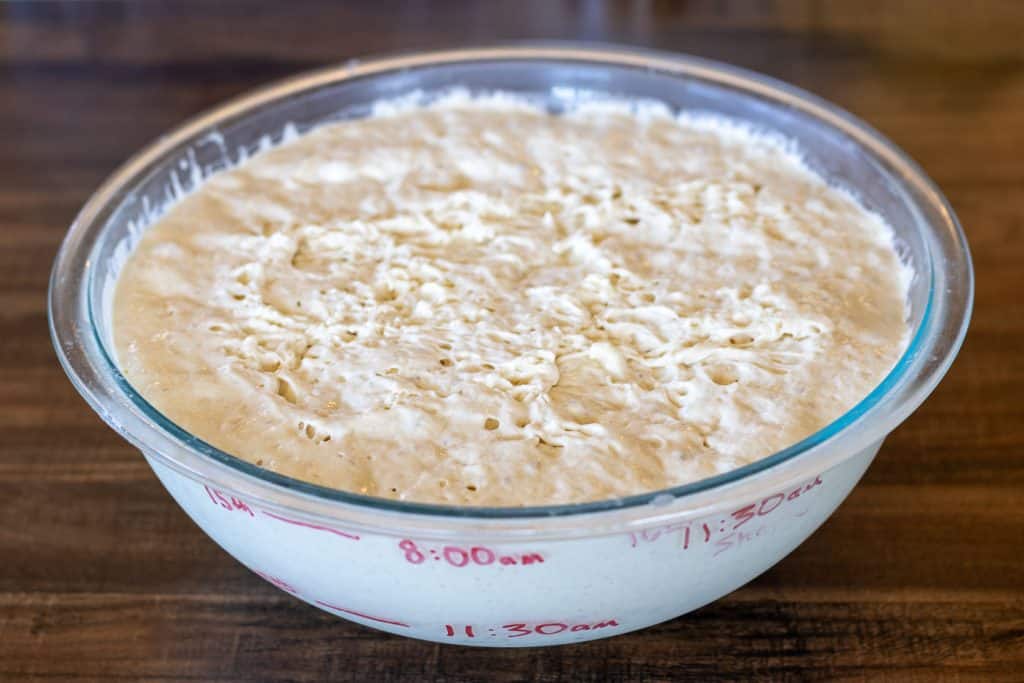 A bowl of long fermented sourdough dough in a large glass bowl with the rise times written on the bowl.