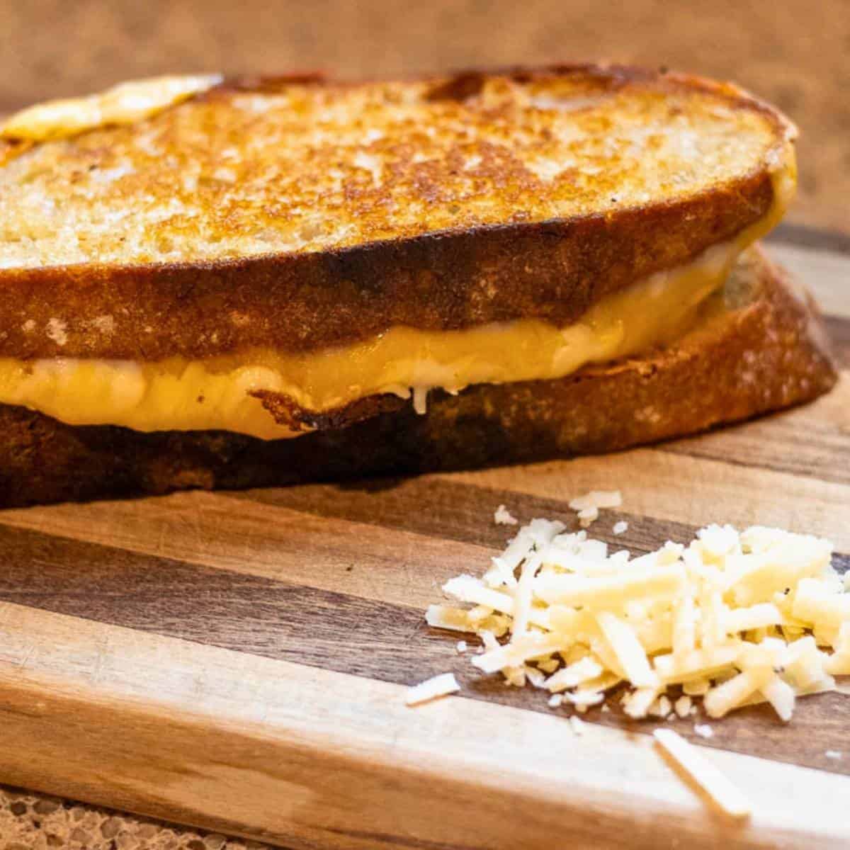 A sourdough grilled cheese sandwich on a cutting board with a bit of shredded cheese.