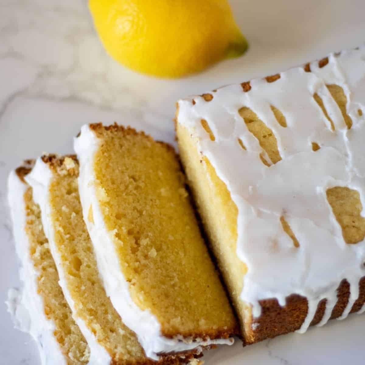 A loaf of sourdough lemon cake sliced up with lemon icing drizzled on and a whole lemon next to it.