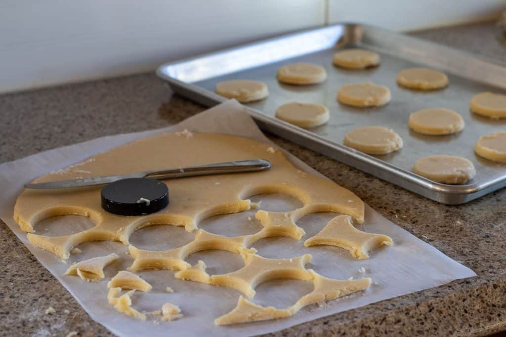 Lemon shortbread cookies being cut out and placed on a baking sheet prior to baking.