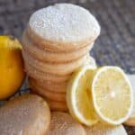 A stack of sourdough shortbread lemon cookies with two slices of lemon on a wire rack.