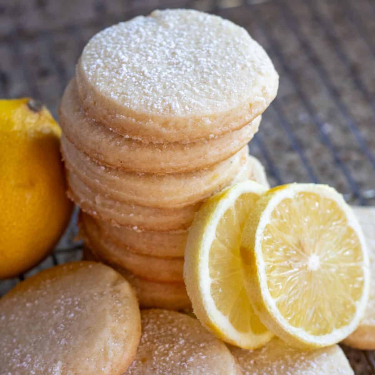 A stack of sourdough shortbread lemon cookies with two slices of lemon on a wire rack.