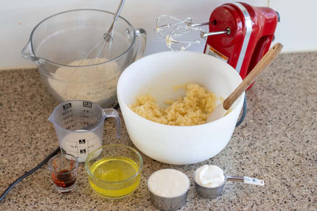 All the ingredients for sourdough vanilla cupcakes on a counter with a handheld mixer.