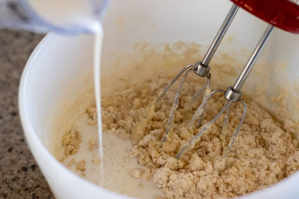 Sourdough cupcake batter being mixed up in a white bowl by a handheld mixer.