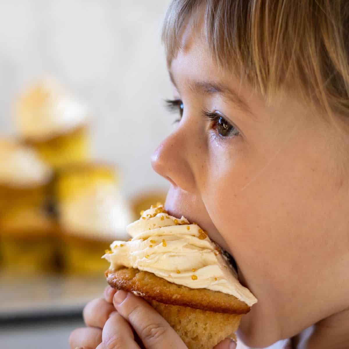 A little girl biting into a sourdough vanilla cupcake.