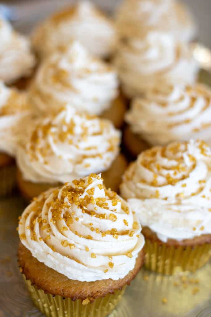 A batch of frosted sourdough vanilla cupcakes with gold sprinkles.