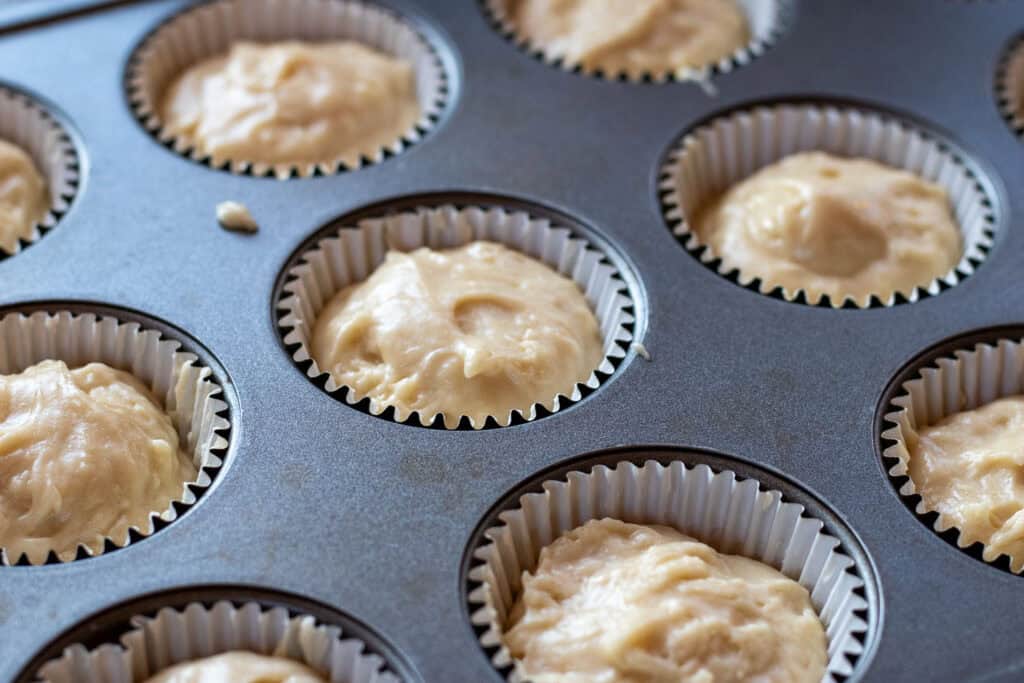 A muffin tin filled with cupcake liners 2/3rds full of unbaked cupcake batter.