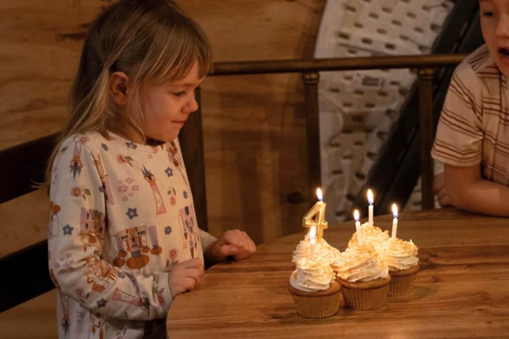 A little girl getting ready to blow out the birthday candles on her frosted cupcakes.