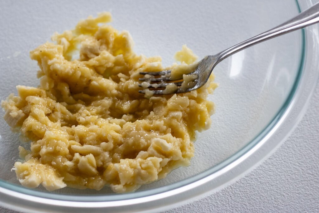 A bowl with mashed bananas in it with a fork pressing into it.