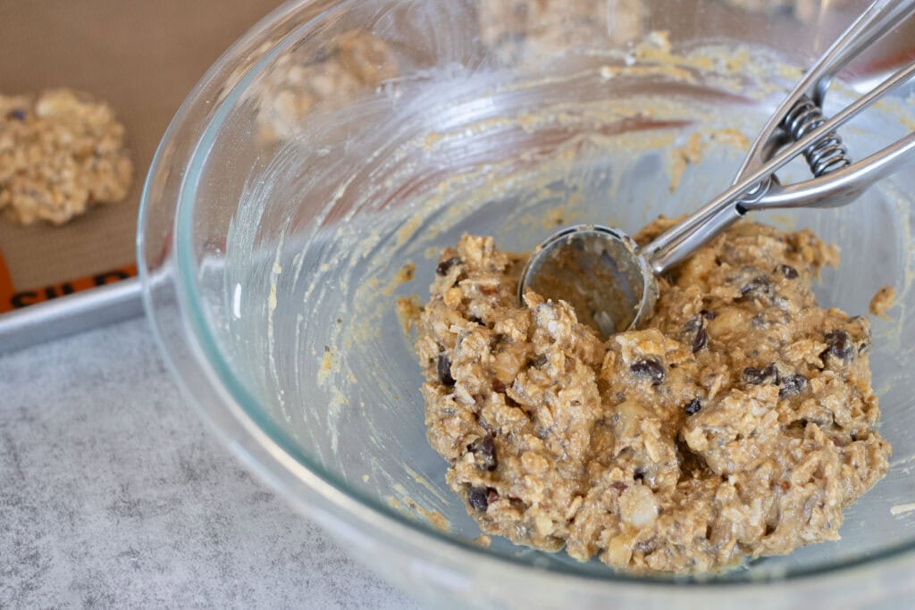A bowl of sourdough breakfast cookie dough batter and a medium cookie scoop.