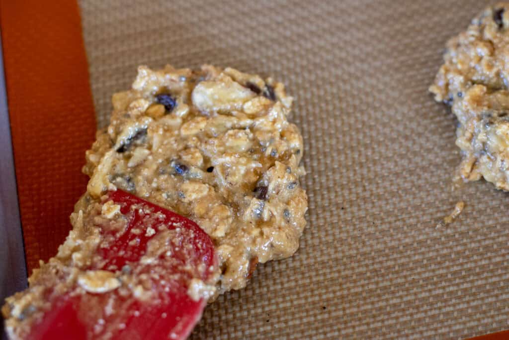 A red silicone spatula pressing down a scoop of breakfast cookie dough ball batter.