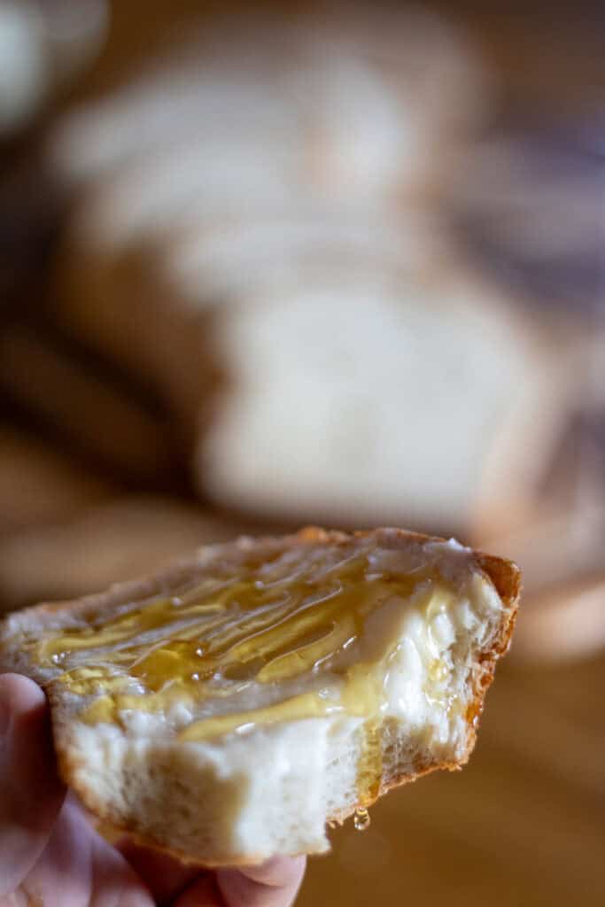 A woman holding a slice of old fashioned white sandwich bread slathered in butter and drizzled with honey.