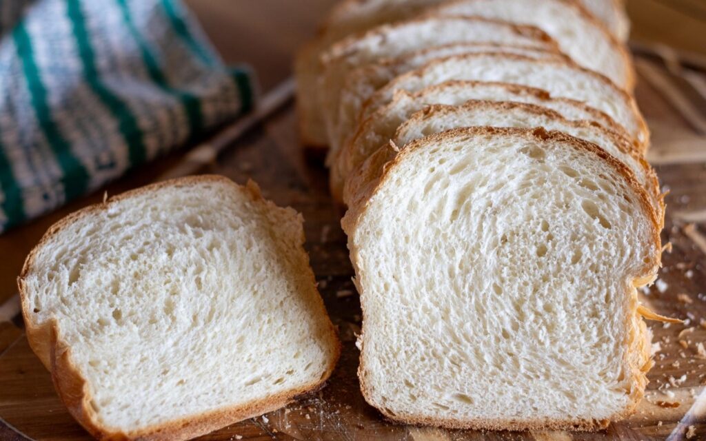 A sliced loaf of white sandwich bread on a cutting board.