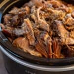 A crock pot full of slow cooked mexican pork shoulder roast with seasonings on top.