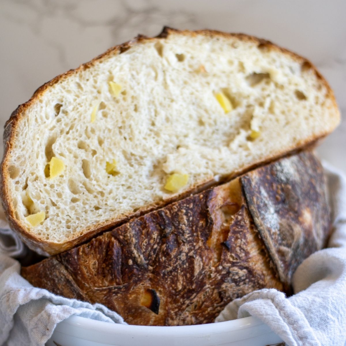 A sourdough apple bread boule sliced in half and stacked with the top half showing the crumb and the bottom half showing the crust, with chunks of fresh apple inside the bread.