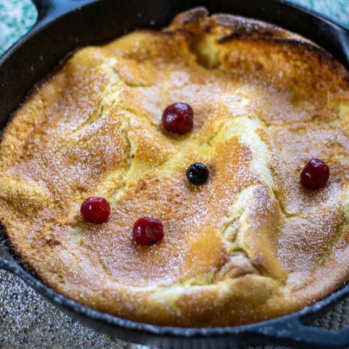 Golden sourdough German pancake baked in a cast iron skillet, topped with powdered sugar and berries
