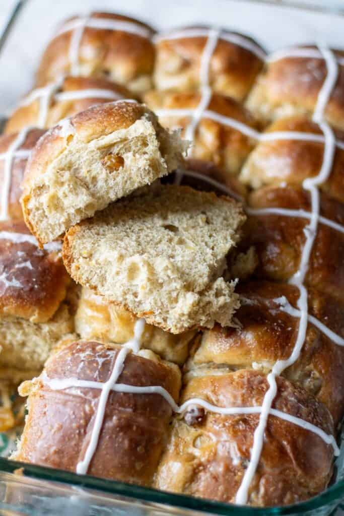 Freshly baked sourdough hot cross buns with golden raisins and icing crosses, one bun torn open to show the soft, fluffy crumb texture inside.