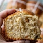 A close up view of a woman holding a large fluffy sourdough hot cross bun.