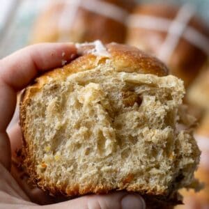 A close up view of a woman holding a large fluffy sourdough hot cross bun.