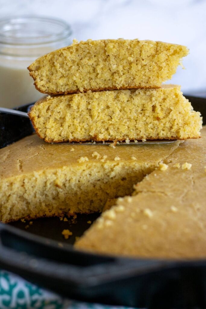 Stacked slices of sourdough cornbread with a jar of milk in the background.