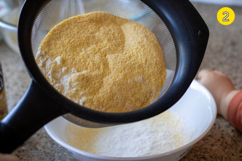 Sifting cornmeal and flour together into a mixing bowl.