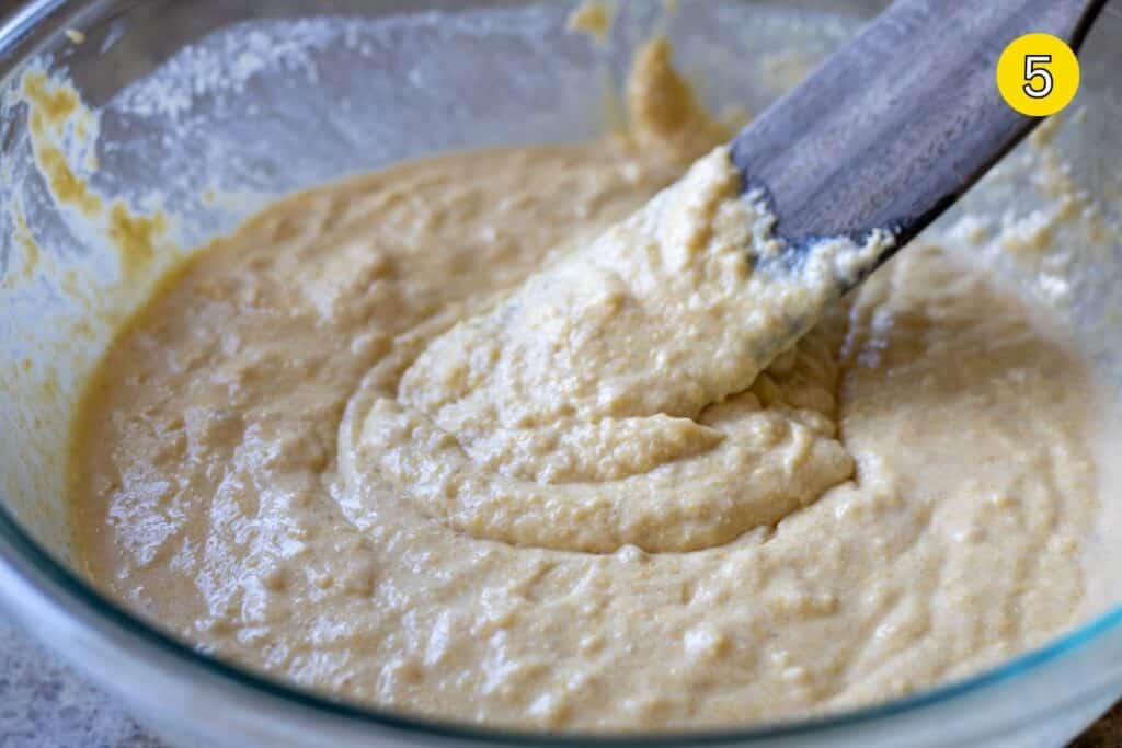 Cornbread batter fully mixed, with a spatula resting in the bowl.