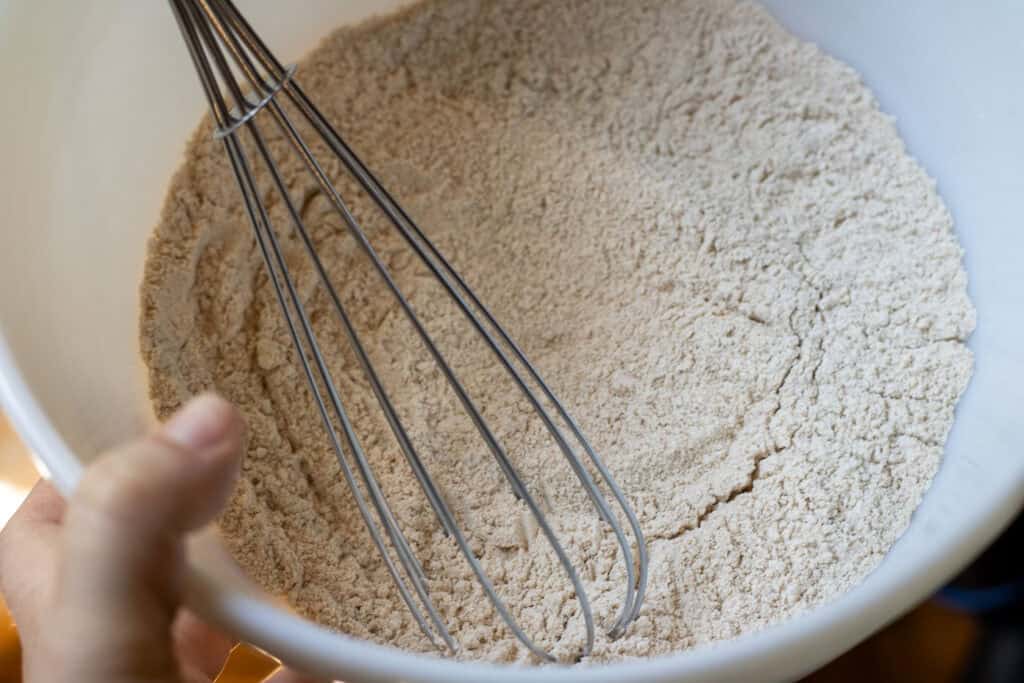 Whisking whole wheat flour and baking powder in a white mixing bowl.