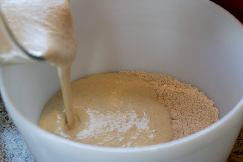 Pouring blended pancake batter into a bowl of flour mixture.