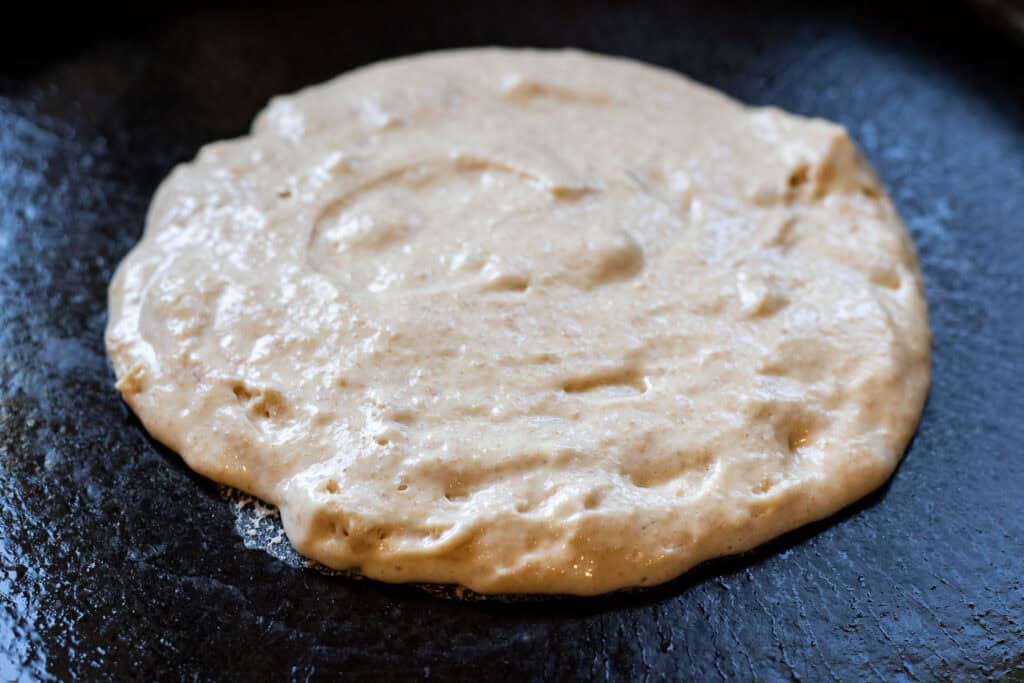 Raw sourdough pancake batter spread into a round shape in a hot skillet