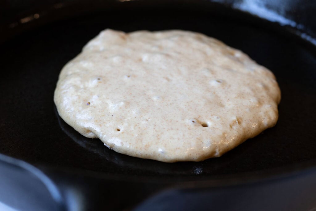 Pancake with bubbles on top cooking in skillet, ready to be flipped