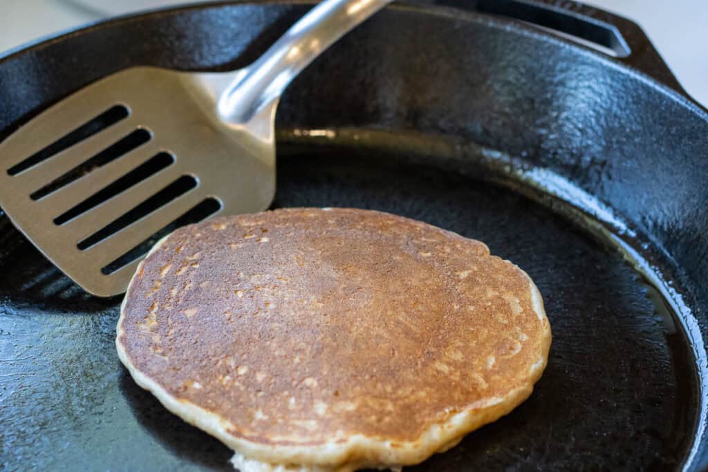Golden-brown pancake in cast iron skillet with spatula ready to lift