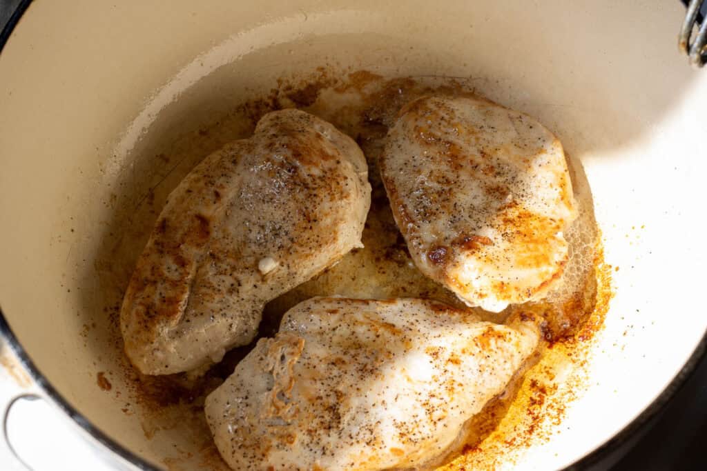 Chicken breasts browning in a Dutch oven with golden bits of fond forming in the pan.